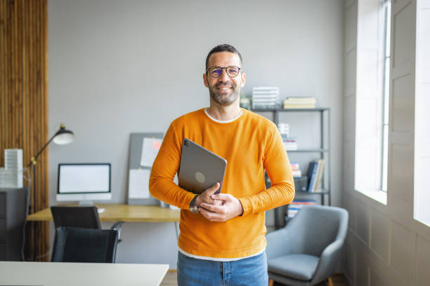 Smiling businessman holding a laptop in a modern office, discussing IFZA Free Zone license costs.